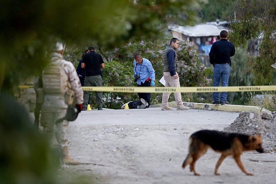 A crime scene investigator with the victim in the lower income neighborhood of Colonia Camino Verde, at the scene of a recent drug cartel homicide in Tijuana, Baja Calif., on April 11, 2017. A drug trafficker message by the New Generation Tijuana Cartel was left on the body.  (Gary Coronado/Los Angeles Times/TNS)