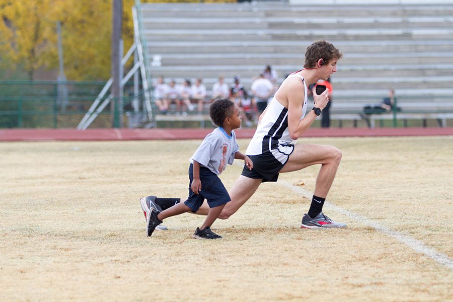 Senior Jonathan Green warms up for the annual Dash 4 Cash, while a participating child follows behind.