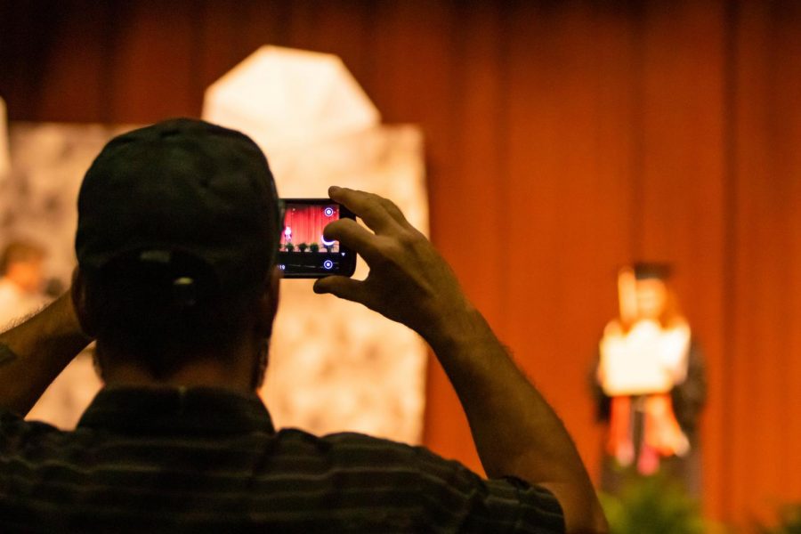 One of the six family members of a graduate snaps a photo while shes on stage. While the situation occurring isnt ideal, families are able to have a more personal experience with one another. 