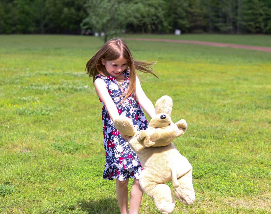 A young girl plays outside with her stuffed bear. Childlike games are often forgotten as people grow and mature.