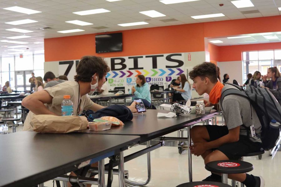 Two unmasked students lean over the table to talk to each other. Despite the spaced out seating, students are still finding a way to break the system. 