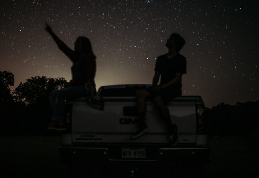 Two teens sit on the bed of a truck while star gazing. Zodiac signs play an important role in many  peoples lives. 