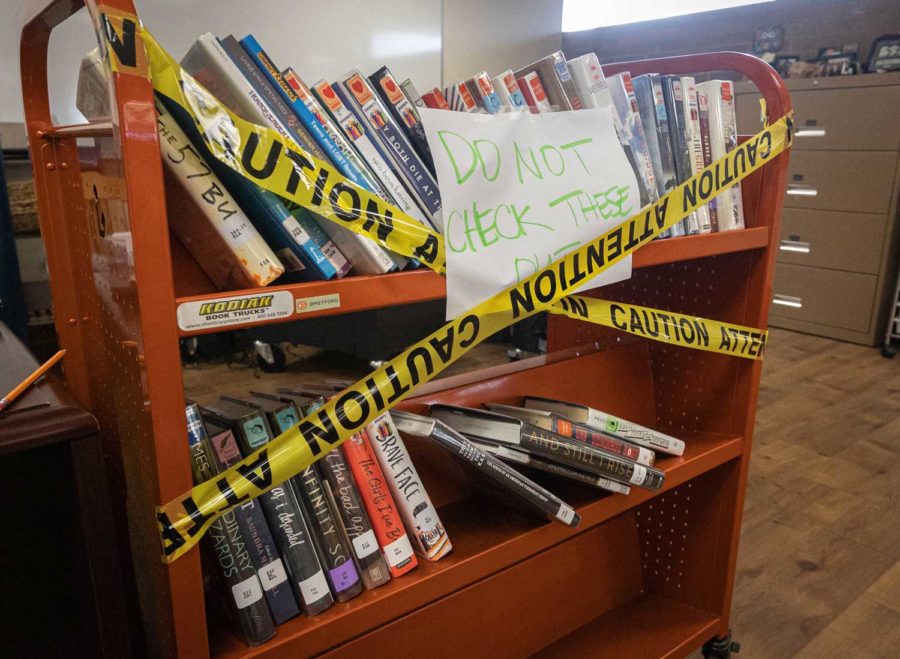 Books sit on a cart apart from the rest of the library texts with a note to students. TISD removed the books from the library on Sept. 28, 2022 as part of a review for educational suitability.