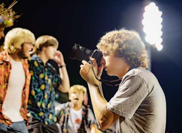 Holding a camera in his hand, Junior Caden Jackson takes pictures of the student section at a football game on Aug. 24, 2023.