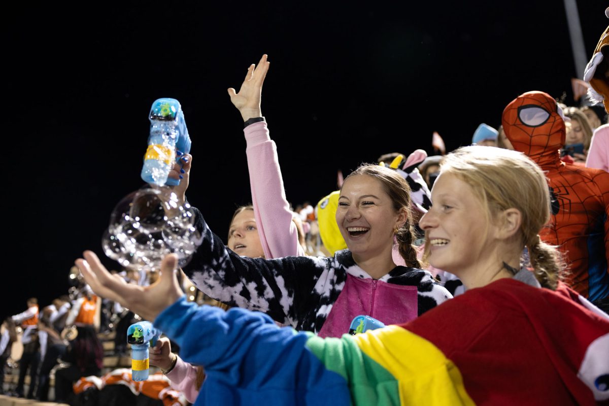 Senior Annbeth Killian and Sadie Mitchell smile as they use a bubble machine in the student section. The student section theme was We are number one, and students dressed in onesies as a first round tradition.