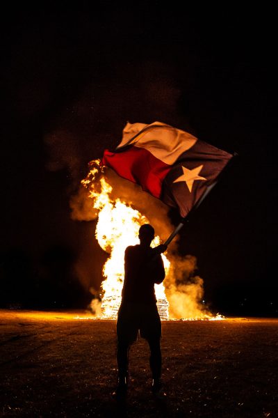 A student waves a Texas flag in front of the annual bonfire. the bonfire was a tradition until 2021, and has not been done since then. 
